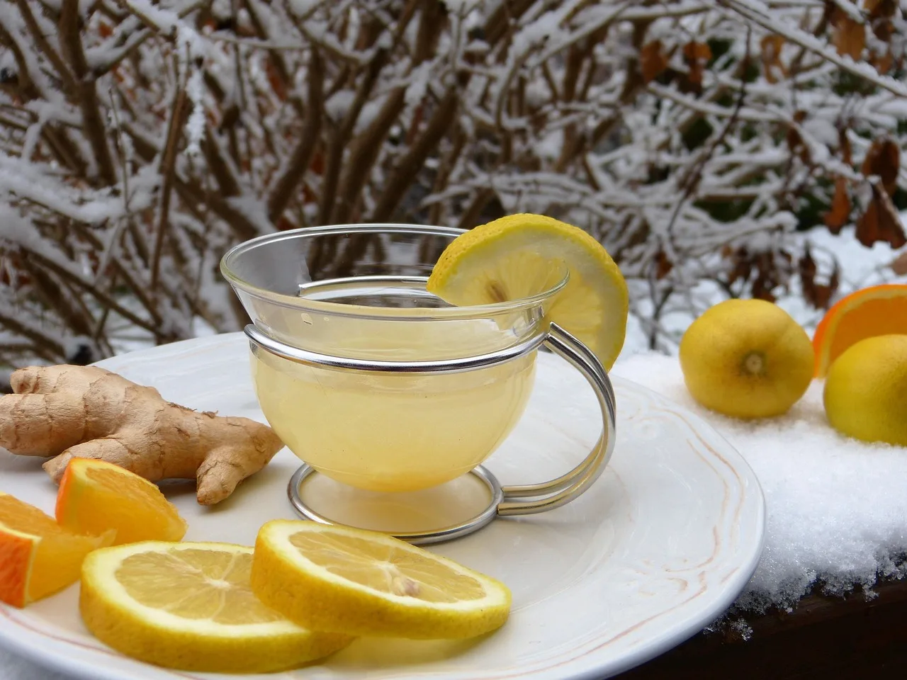 Bevanda di acqua con limone e zenzero in un bicchiere trasparente su sfondo bianco.